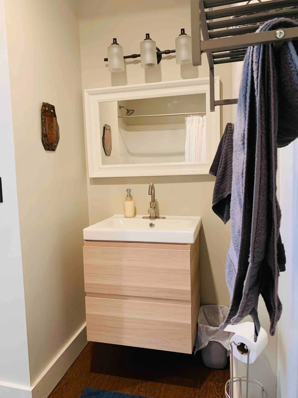 A modern bathroom with a stylish sink, sleek light fixtures, a large mirror, and a wooden storage unit. The space feels fresh and uncluttered, designed for relaxation and personal care.