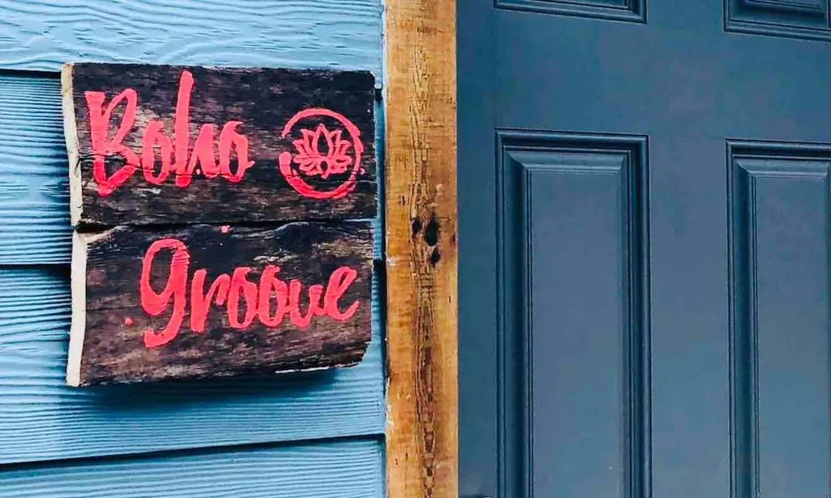 This image features a wooden sign with the text 'Boho Groove' and a lotus symbol, set in an inviting, artistic environment. The sign serves as a visual cue for arrival and welcomes travelers to the property, while the background hints at a communal or shared space ideal for socializing or brief stops.