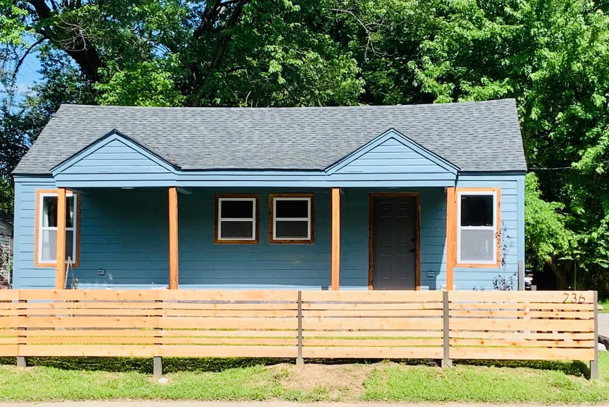 This image features the blue exterior of the house, framed by a wooden fence and a welcoming front porch. The scene suggests a secure, inviting space for families and highlights the openness of the fenced front yard, perfect for enjoying morning coffee or watching children at play.