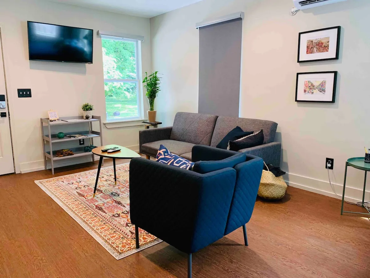 A spacious living room featuring a sofa and armchair set around a coffee table and decorative rug. Wall artwork and a television add both personality and entertainment options. The arrangement encourages conversation and shared activities, with soft lighting contributing to a comfortable, inviting feel.