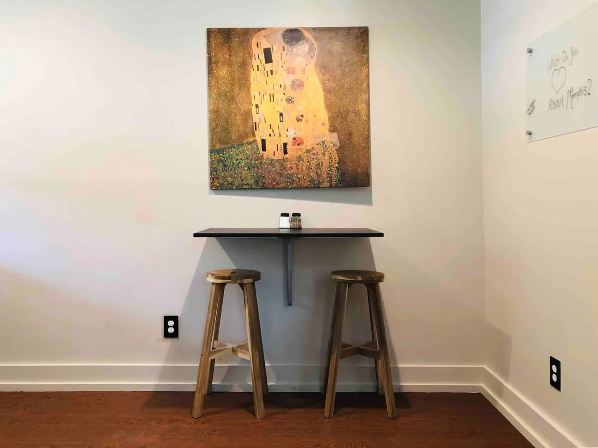 A minimalist dining nook with a small table and stools, accented by abstract wall art and simple salt and pepper shakers. The nook exudes intimacy and relaxation, inviting quiet meals or coffee breaks.